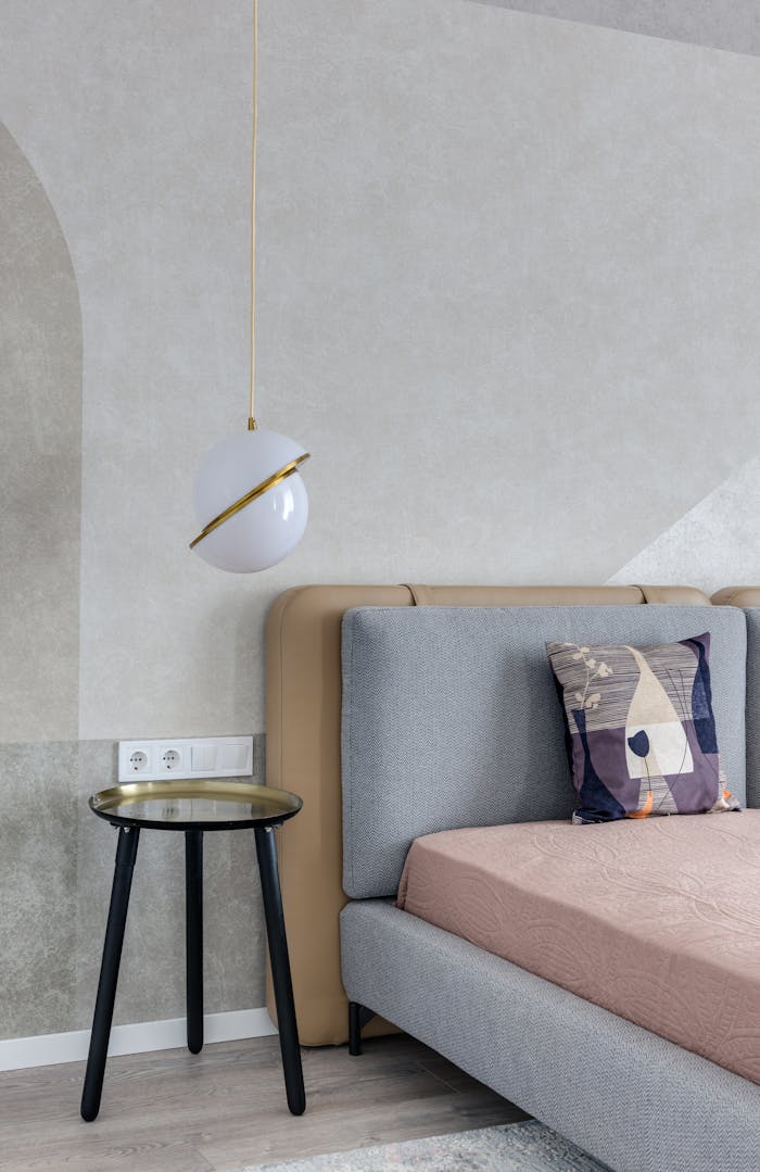 heros-img Comfortable bed with colorful pillow near bedside table under lamp with creative design